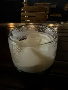 A partially finished Guinness pint glass with foam clinging to the inside, sitting on a dark wooden pub table with blurred wooden chairs in the background.