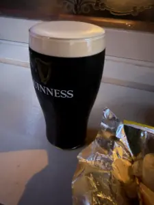 A Guinness pint glass with a creamy head sits on a counter next to an open bag of potato chips, evoking the relaxed atmosphere of a cozy pub.